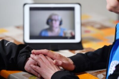 Zu sehen ist eine mögliche Verbindung von Beratungs und Technik mit zwei Menschen im Gespräch im Vordergrund und einer dritten Person im Hintergrund, die per Videokonferenz dazugeschaltet ist.
